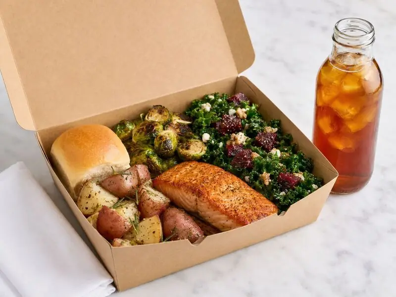 San Mateo Catering Company individually boxed dinner arranged with salmon, herb potatoes, roasted sprouts, beet-topped kale, and tea.