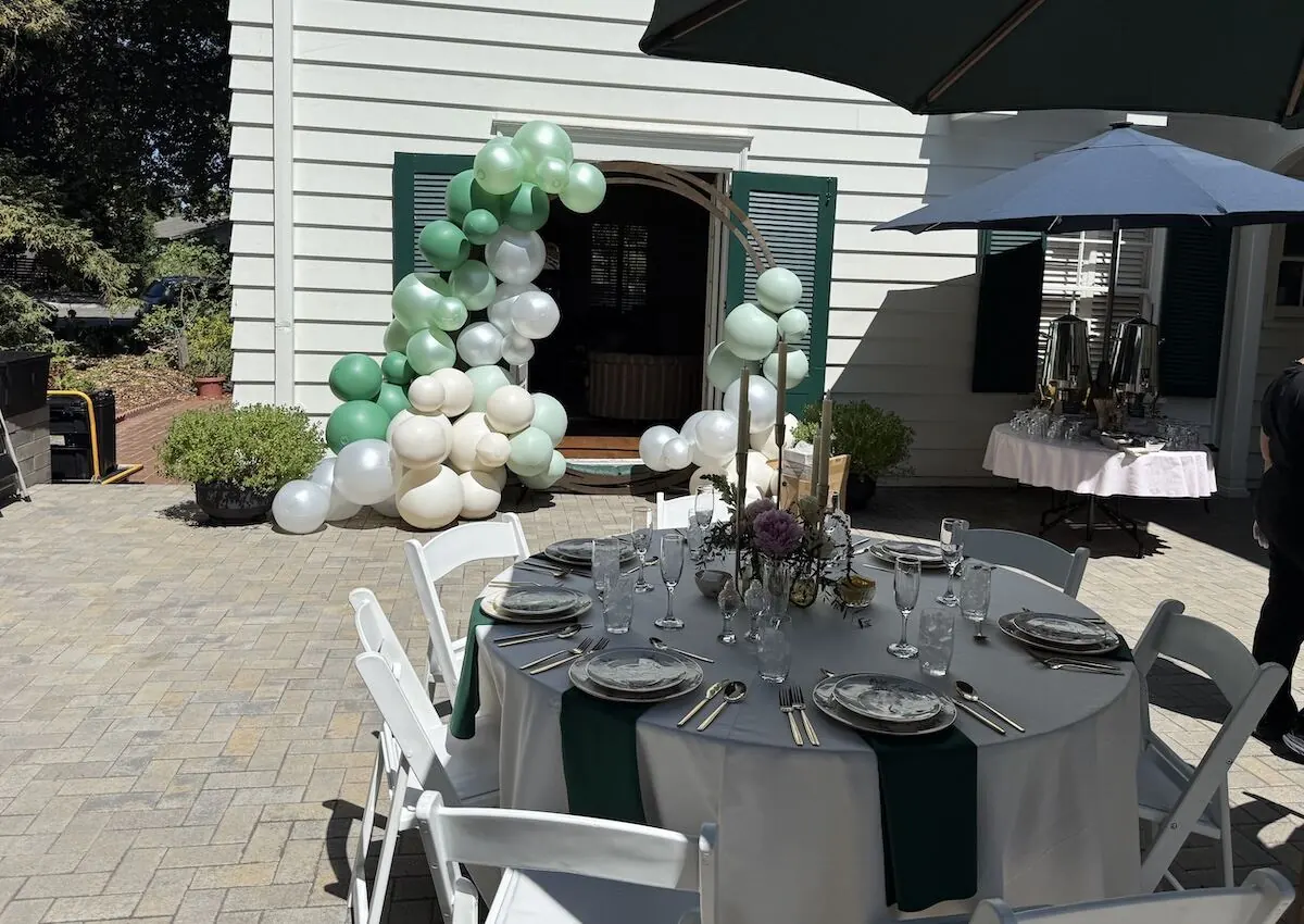 Sage and ivory balloon garland over a doorway paired with a bloom-accented tablescape — balloon and floral styling for Millbrae catering celebrations