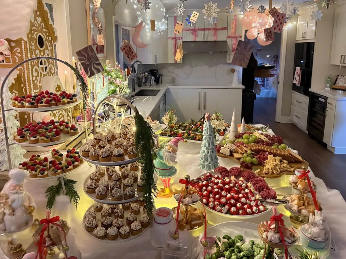 Themed party tablescape where tiered tarts and cupcakes sit under pastel balloons with fresh blossoms tucked between them — floral party styling for Burlingame catering