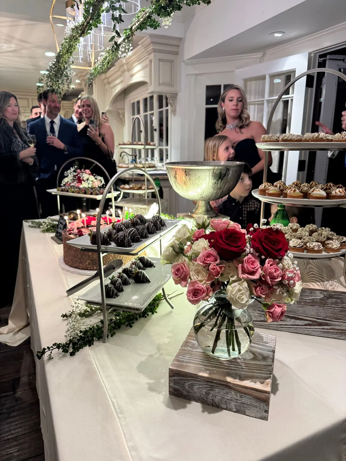 Reception sweets table of chocolate-shelled berries and petite pastries ringed with fresh garden roses — wedding dessert florals for Redwood City catering