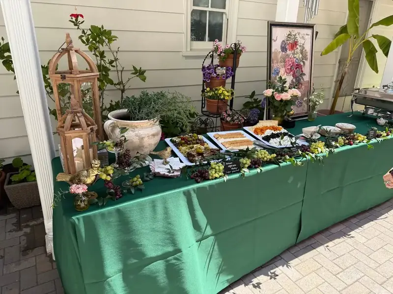 San Mateo backyard catering buffet arranged with assorted appetizers, grapes, crackers, flowers, and decorative garden elements.