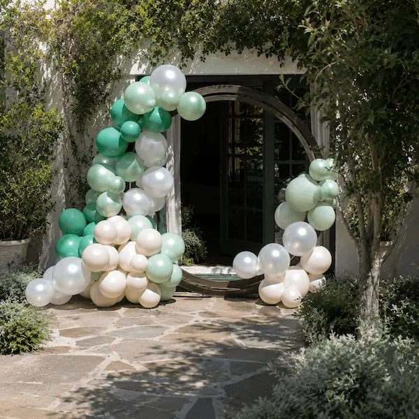 Sage green, mint, and white balloon arch over an arched garden doorway above an elegantly set table